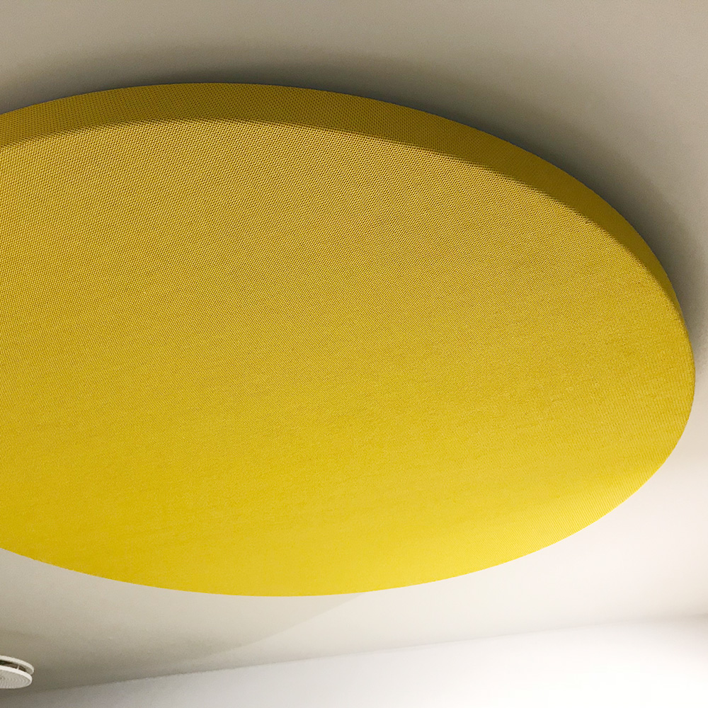 Acoustique et bruit 17 Gros plan sur un grand panneau acoustique de plafond rond et jaune, recouvert d'un revêtement textile, monté directement sur un plafond clair