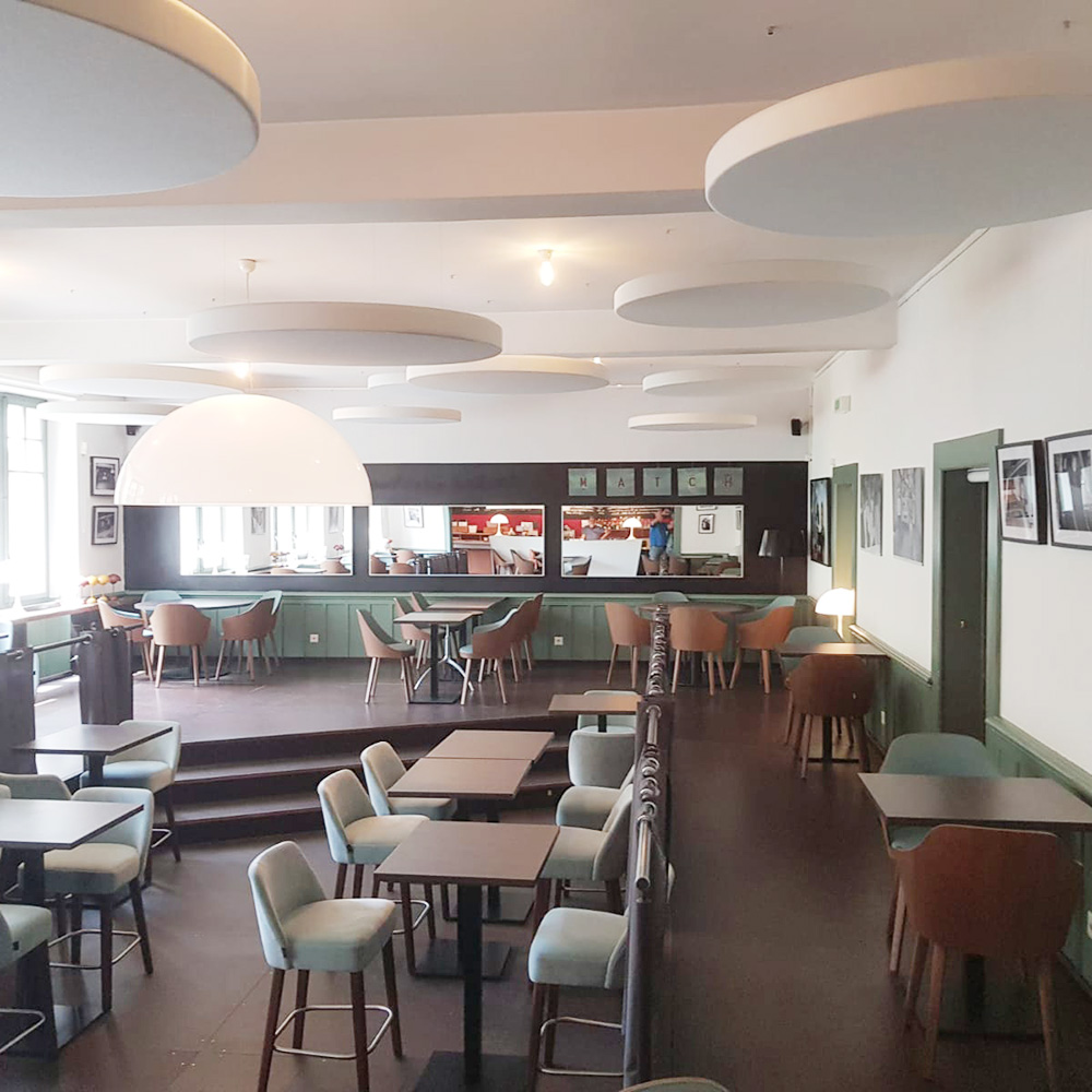 Restauration & Hôtellerie 16 De nombreux panneaux acoustiques ronds et blancs de différentes tailles, suspendus par des câbles, dans une grande cafétéria aux murs lambrissés de vert