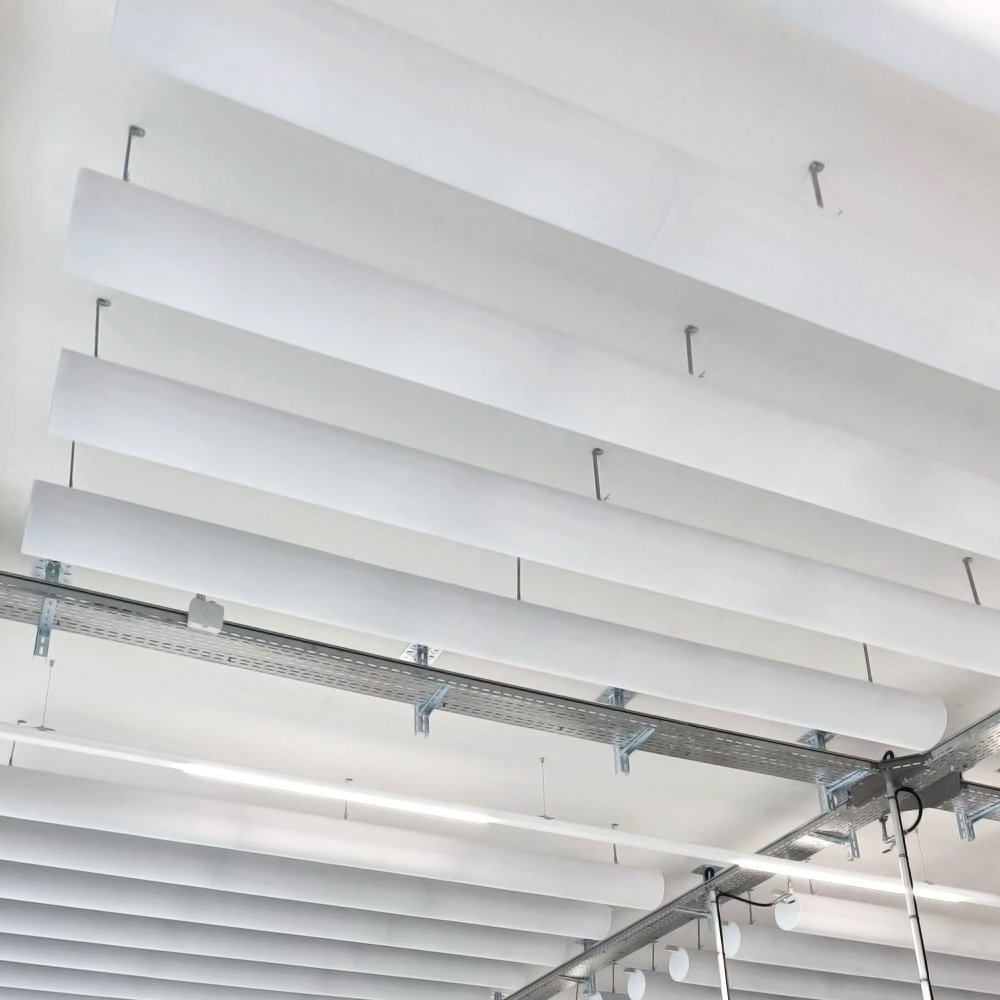 Industrie & Gewerbe 18 Deckenabsorber in Form von weissen Zylindern horizontal in Reihen an einer Decke abgehängt