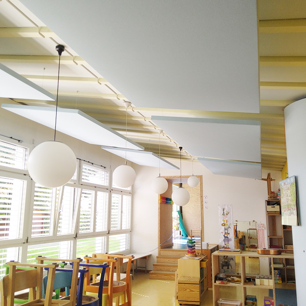 Schule & Bildung 18 Grosse weisse Akustik-Deckenpanels abgehängt an schräger Deckenkonstruktion in hellem Kindergartenraum mit Kugelleuchten
