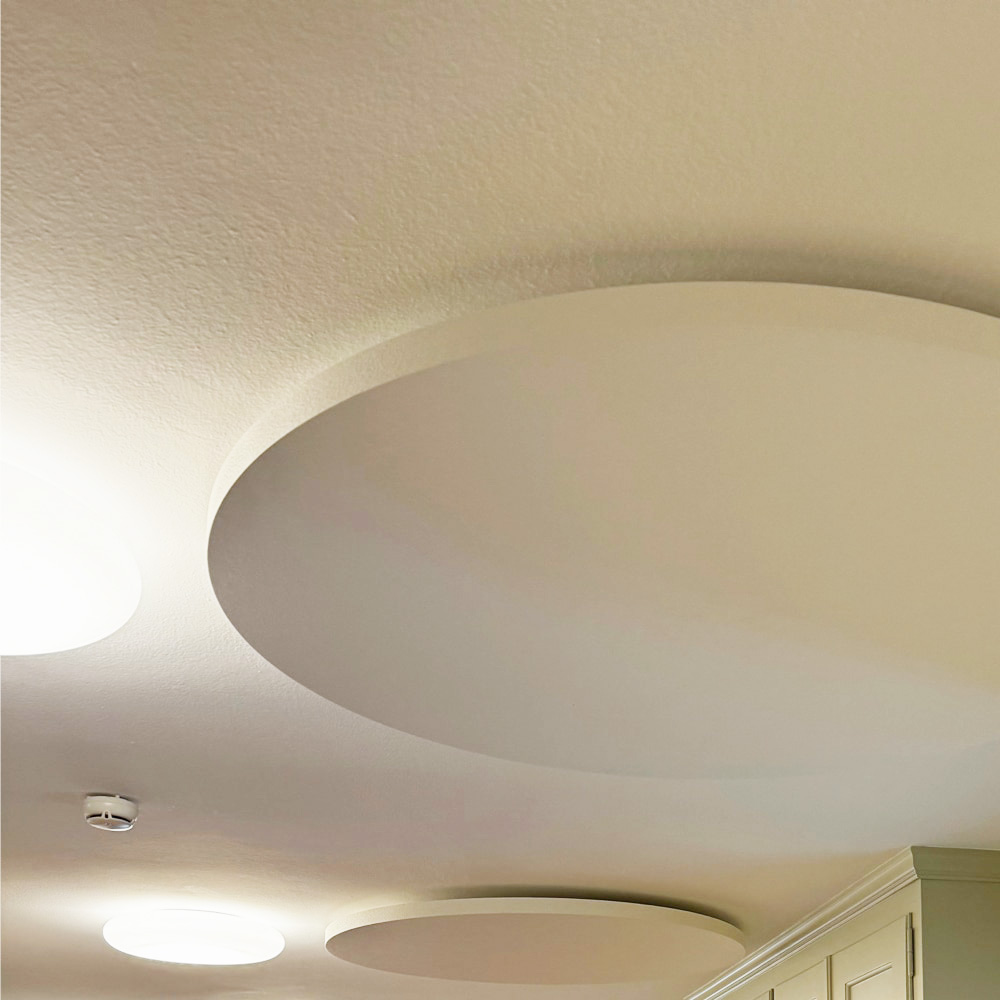 Panneaux incombustibles NoFlame Solo 4 Plusieurs panneaux acoustiques ronds ininflammables, entre lesquels sont suspendus des luminaires suspendus blanc chaud, sur le plafond texturé du restaurant