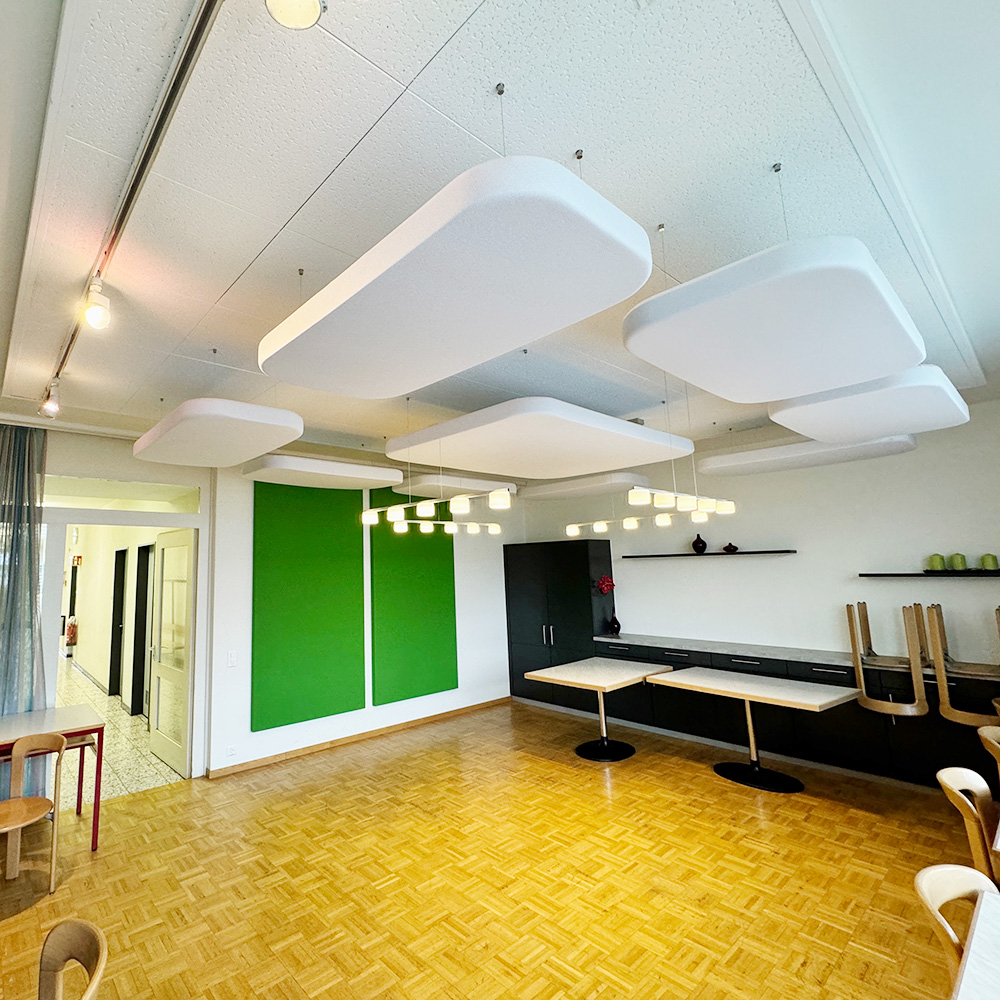Weisse gerundete Akustik-Deckenpanels abgehängt und grüne Wandpanels an Wand in heller Schulaula mit Parkett
