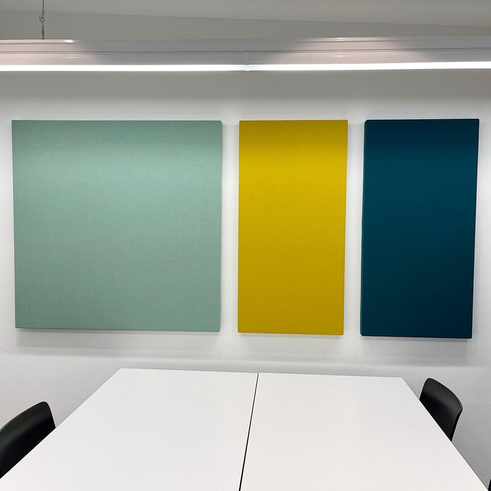 Acoustique et bruit 19 Trois panneaux muraux acoustiques, de couleur vert menthe, jaune et bleu pétrole, disposés côte à côte sur un mur blanc, au-dessus d'une table de conférence blanche, dans une salle de réunion moderne