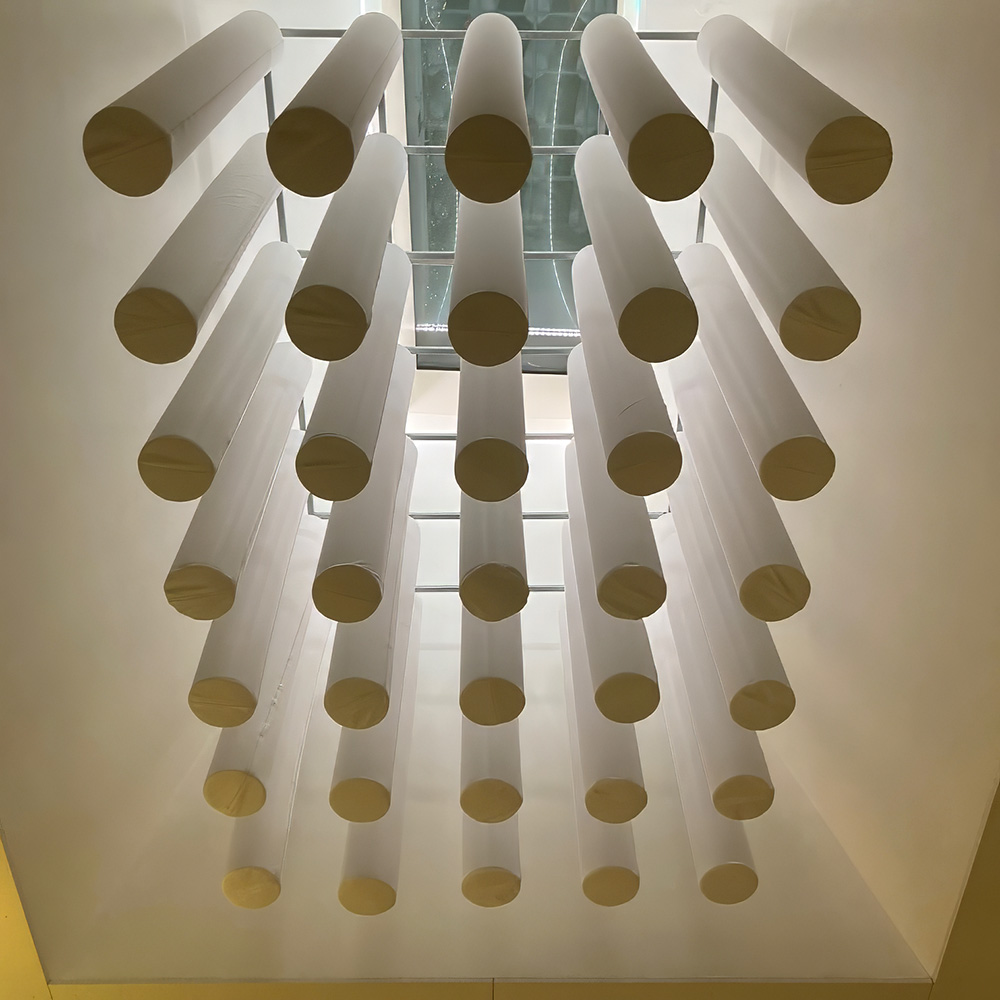 acouFoam Zylinderabsorber 1 Viele weisse Zylinderabsorber in Rasteranordnung auf Trägerstruktur von unten fotografiert vor hellem Fenster