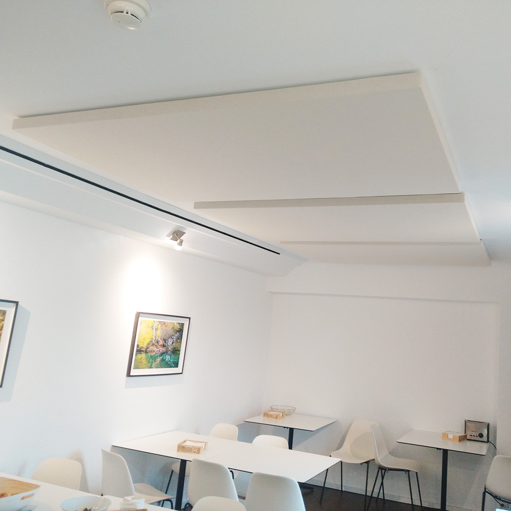 Protection contre l'incendie dans l'acoustique des salles. 19 Trois panneaux acoustiques rectangulaires blancs, légèrement suspendus, dans une salle de séjour lumineuse équipée de chaises blanches et de tableaux muraux