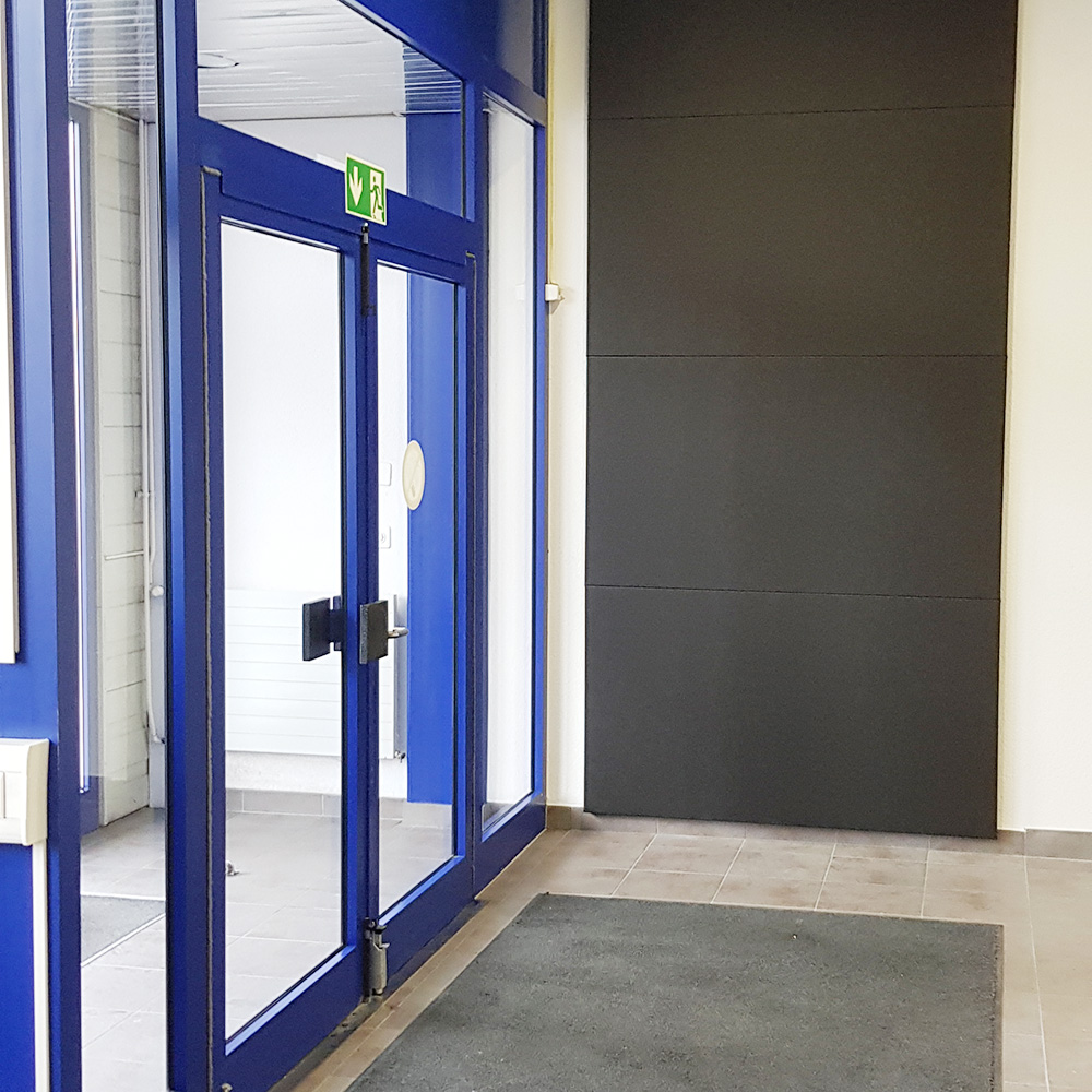 Protection contre l'incendie dans l'acoustique des salles. 21 De grands panneaux muraux absorbants ininflammables de couleur gris foncé, situés à côté d'une porte vitrée bleue portant un panneau « Sortie de secours » dans le hall d'entrée