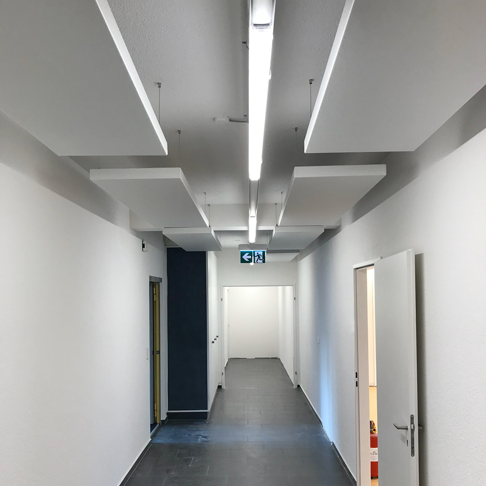 Protection contre l'incendie dans l'acoustique des salles. 1 Des panneaux acoustiques blancs ininflammables, suspendus de manière décalée, dans un long couloir doté d'une sortie de secours