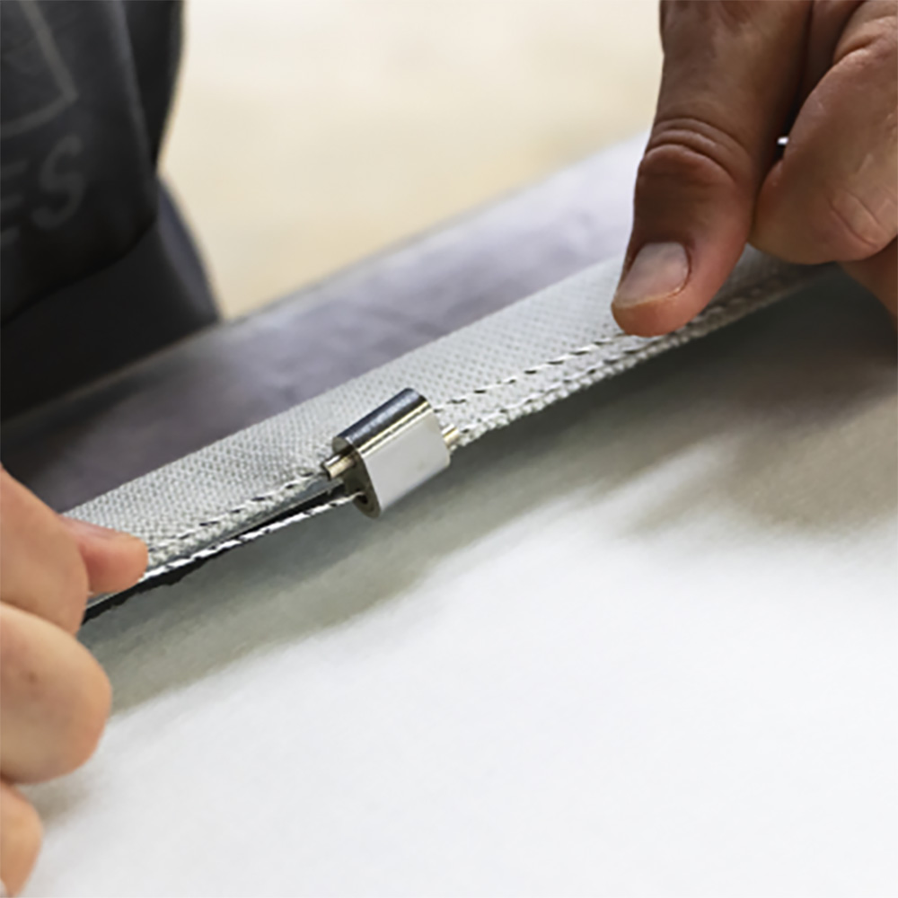 Développement durable et recyclage 18 Gros plan sur des mains en train de changer la housse textile grise d'un panneau acoustique, avec un système de fixation à boutons-pression visible et un absorbeur blanc en dessous
